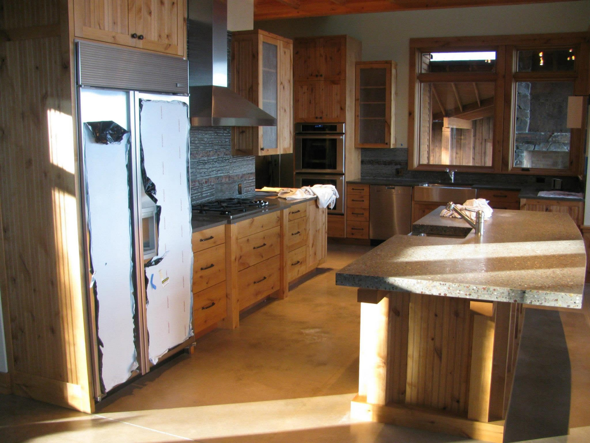 Knotty alder kitchen with concrete island and paneled refrigerator